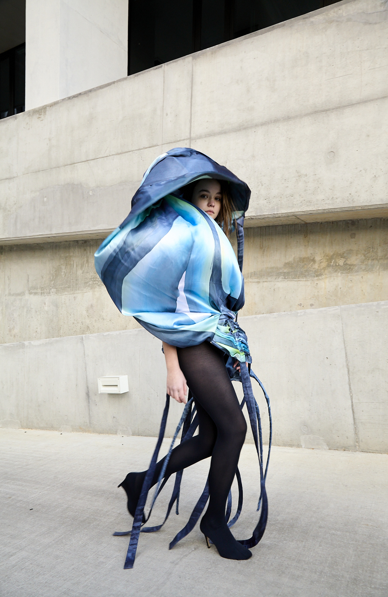 Figure wearing a blue design in front of concrete architecture